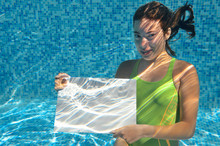 Beautiful Young Girl Holding White Blank Board In Swimming Pool Under Water, Fitness And Fun On Family Vacation
