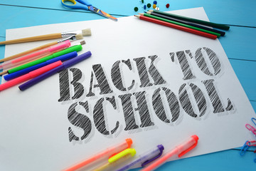 Wall Mural - The text Back to school on a sheet of paper on the table with school accessories (pens, pencils, brushes)