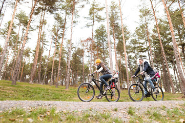 Wall Mural - Young family in warm clothes cycling in autumn park