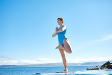 Cheerful Sportive Woman In Yoga Pose On Edge Of Pool Looking Away On Background Of Sea, Iceland.