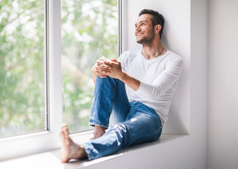 Wall Mural - Handsome smiling man relaxing on window sill