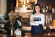 © weedezign - Asian female barista wear jean apron crossed her arms at counter bar with smile face,cafe service concept,owner business start up