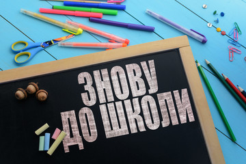 Wall Mural - The text Back to school (ukrainian language) on a black chalkboard on the table with school accessories (pens, pencils, brushes)