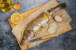  Preparation of fresh fish for baking. Raw zander, lemon and onion on a kitchen cutting board on a dark background.