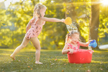 The Cute Little Blond Girls Playing With Water Splashes On The Field In Summer