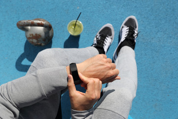 Gym man touching smartwatch screen during workout strength training. Top view from above: kettlebell weights, green smoothie, body and legs. POV of athlete sitting resting. Healthy fitness lifestyle.