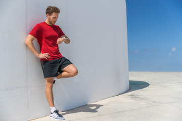 Wall Mural - Smartwatch runner man checking progress on smart fitness sport watch during running break cardio workout training. Athlete relaxing using online app on wearable device. Outdoor active lifestyle.