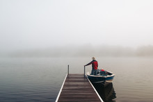 Man Standing With Boat Near A Dock On Foggy Lake.