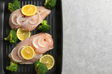 Frying pan with raw chicken breasts, lemon and broccoli on table