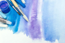 Paintbrushes With Paint And Pastel Crayons On Blue Watercolor Background With Paper Texture