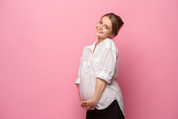 Wall Mural - Young beautiful pregnant woman standing on pink background