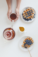 Wall Mural - top view of delicious breakfast of waffles and tea in female hands