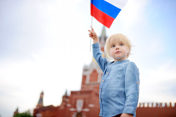 Wall Mural - Cute little boy with russian flag with Spasskaya tower (Russia, Moscow) on background