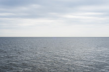 The Calm Blue-gray Ocean Waters Meet The Cool, Cloudy Blue Overcast Sky, With A Perfectly Straight Horizon Line.