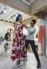 An asian fashion designer is adjusting and fixing a dress on model in the studio