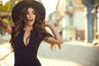 canvas print picture - Portrait of gorgeous glam tattooed lady with long wavy hair and beautiful make up holding her trendy fedora hat for it not to be blown away by the wind. Her mouth open with surprise. Copy-space