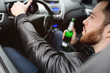 © Evgeniy Kalinovskiy - A young handsome bearded man with a bottle of beer or a low-alcohol drink at the wheel of a car. Driving in a state of intoxication