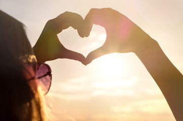 Wall Mural - Woman making heart with hands in sunset. Love symbol in sunny summer night. Happy and carefree lifestyle.