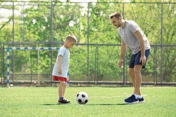 Wall Mural - Father and son playing football on soccer pitch