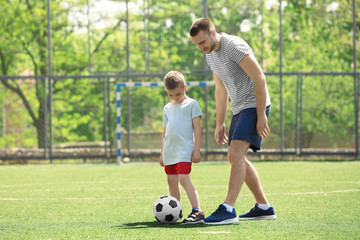 Wall Mural - Father and son playing football on soccer pitch