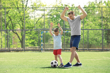 Wall Mural - Father and son playing football on soccer pitch