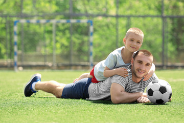 Wall Mural - Father and son with ball lying on soccer pitch