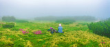 Fototapeta Kuchnia - Woman tourist resting on a mountain meadow among the flowers in the fog