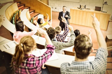 students raising hands with teacher in lecture hall