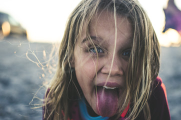 Smiling blonde girl at the beach sticking out tongue