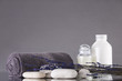 Spa. The towel is rolled up, white pebbles, two bottles of cream. Lavender. The background is gray.