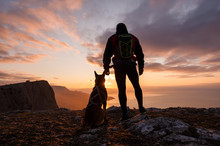 Silhouette Of Young Man With His Dog At Dawn With Sea And Mountain On Background.