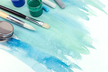 Wall Mural - various paintbrushes, paints and pastel chalks on green blue watercolor background