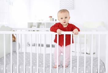 Cute little baby standing in crib at home