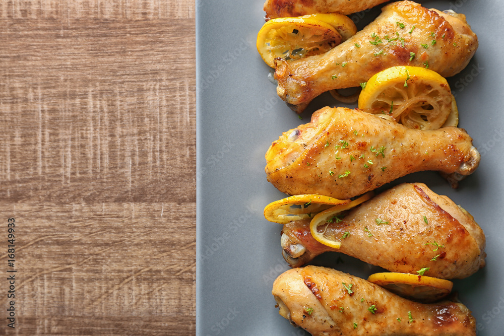 Plate with delicious roasted chicken drumsticks and lemon on wooden table