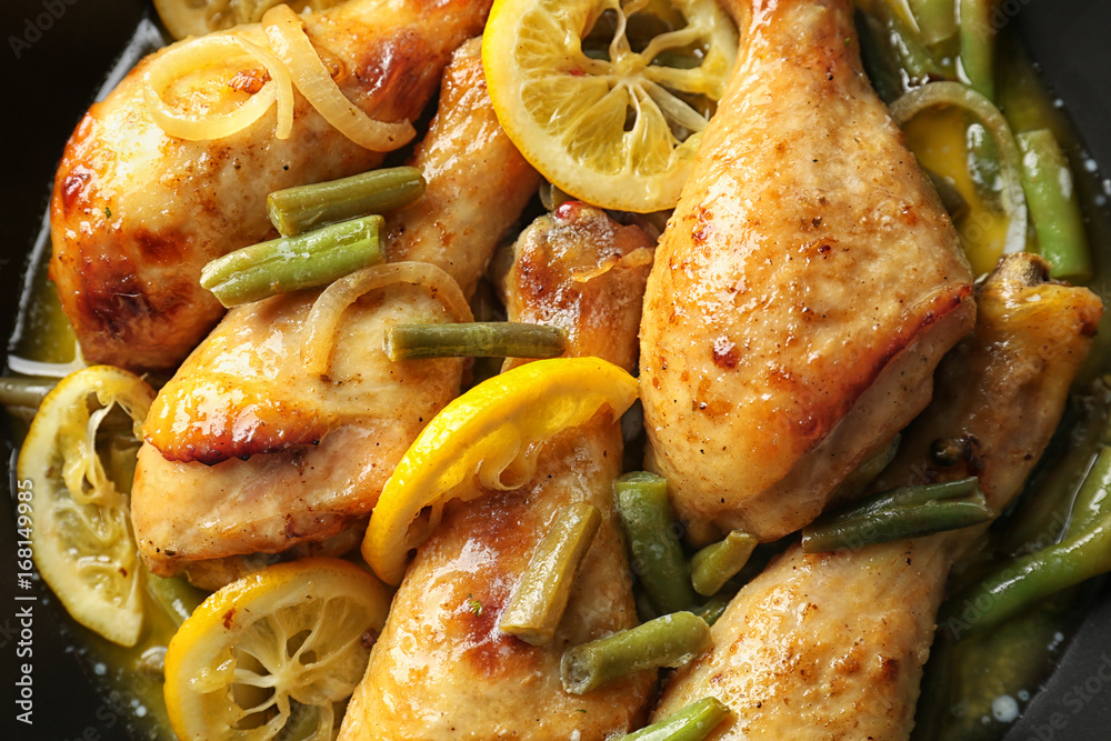 Delicious chicken drumsticks with sliced lemon in frying pan, closeup
