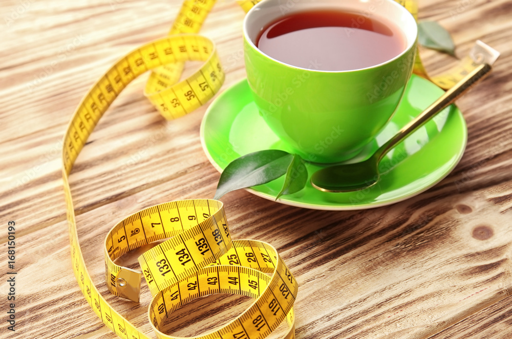 Cup of tea and measuring tape on wooden table. Weight loss concept