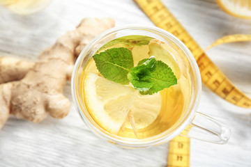 Fototapete - Cup with ginger tea and measuring tape on light table. Weight loss concept