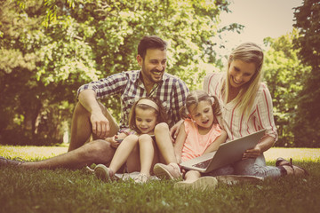 Happy family with two children in meadow using laptop and digital tablet together. Family in meadow.