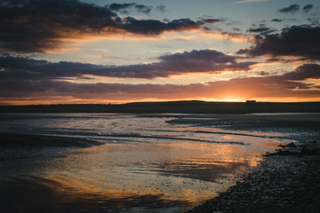 sunset sky colours reflected in wet sand on beach at low tide,