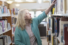 Curious Caucasian Woman Reaching For Book In Library