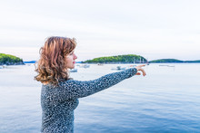 Young Woman Pointing To Boats On Edge Of Dock In Bar Harbor, Maine At Sunset