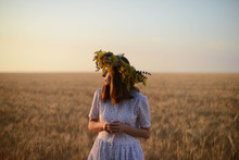 Beautiful Girl In Wreath Of Flowers In Meadow On Sunny Day. Portrait Of Young Beautiful Woman Wearing A Wreath Of Wild Flowers. Young Pagan Slavic Girl Conduct Ceremony On Midsummer. Earth Day