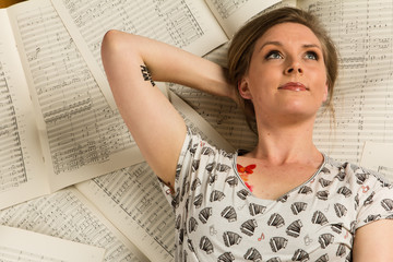 Wall Mural - Young caucasian hipster woman with music shirt lies on sheet music in a room