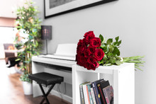 Bouquet Of  Red Roses On The White Table With White Piano In Background
