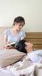 © maewsom15 - Young Asian Man Lying on Lap of Her Wife While Reading A Book and Smiling Each Other,Romantic asian couple is relaxing on bed, soft focus background