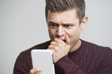 Wall Mural - Cropped portrait of a shocked young man using a smartphone