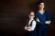 © jpleskachevskaia - Attractive boy keeping his hands crossed while standing near his little sister in big glasses and school uniform. Positive pupils isolated over blank studio background. School, children, learning