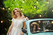 © lanarusfoto - Happy woman in white dress near vintage car, cozy pathway, in the background garland, freedom and goal achievement