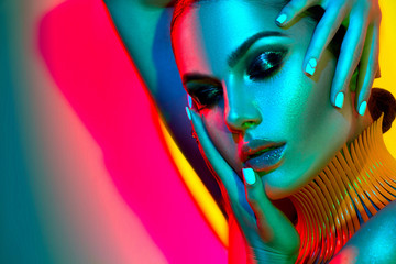 Wall Mural - Fashion model woman in colorful bright lights with trendy makeup and manicure posing in studio