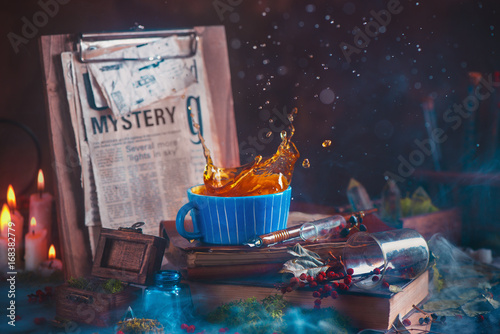 Fotomural Tea splash in a ceramic cup on a wooden background with candles, mystery newspap
